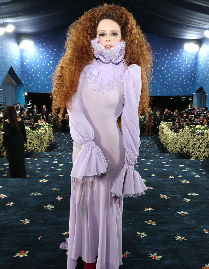 Person with voluminous curly hair wearing a lavender ruffled dress at Met Gala 2025 fashion fails event.