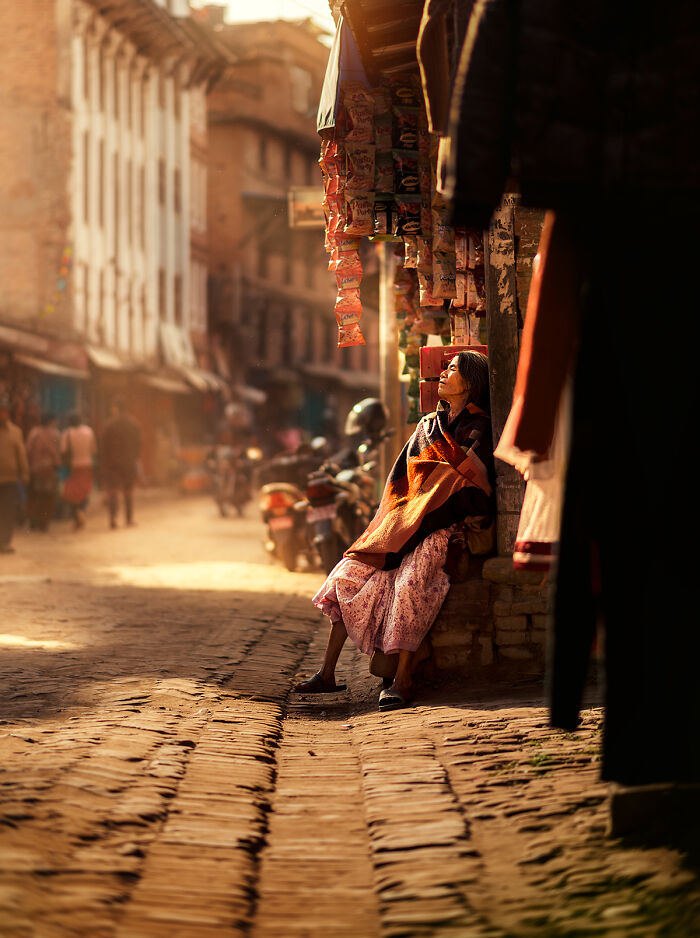 Woman wrapped in a blanket sitting quietly on a street corner during golden hour in a vibrant street photography moment
