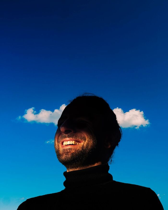 Man smiling with a cloud behind his head resembling horns, a creative photo edit that makes you question reality.