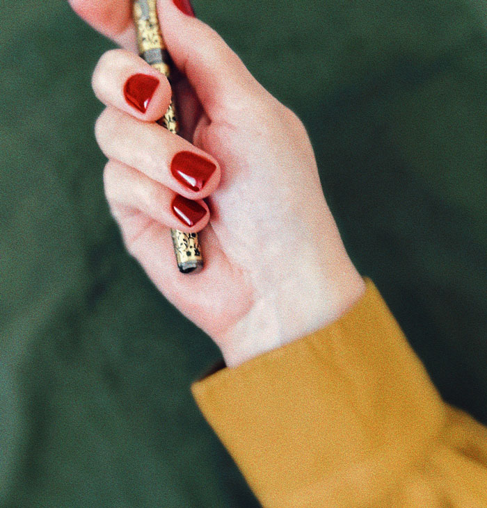 Close-up of a hand with red nails holding a decorative pen, illustrating one weird rule parents had.