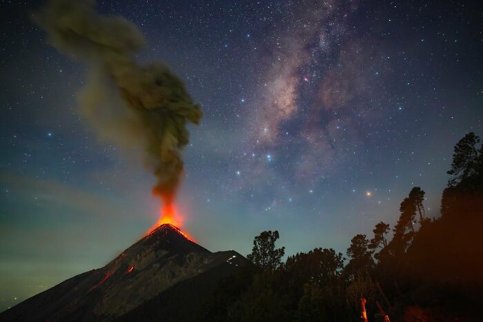Volcanic eruption beneath a vibrant Milky Way sky showcasing the beauty of the night sky with glowing lava and stars.