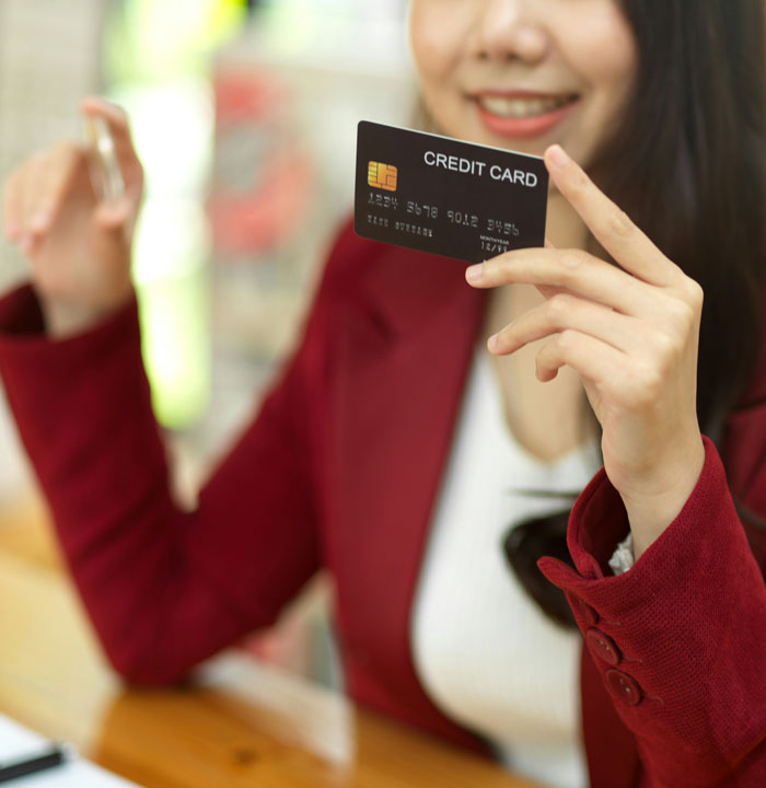 Woman smiling and holding a credit card, illustrating common ways people lose money while thinking they are saving.