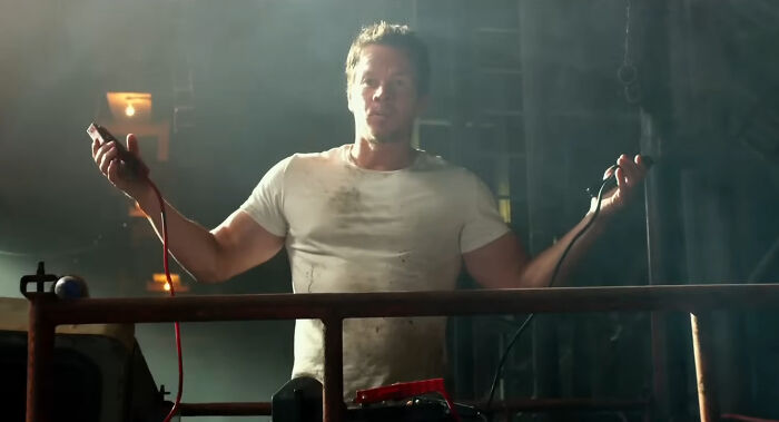 Actor in a dirty white shirt holding jumper cables on an industrial set, related to miscast actors in movies.