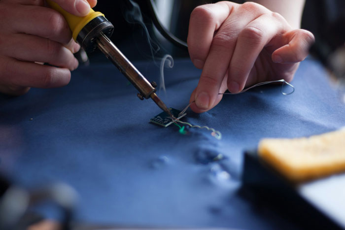 Close-up of hands soldering small electronic components, illustrating a weird habit that means I was raised poor concept.