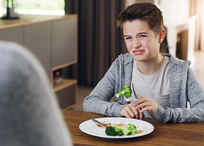 Young boy grimacing at broccoli on plate, illustrating child neglect and food refusal related to CPS intervention concerns.