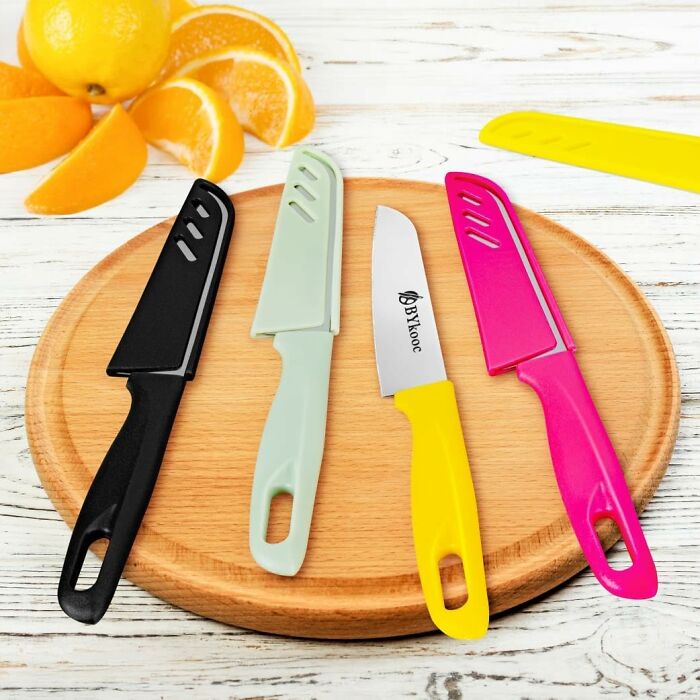Colorful affordable home find kitchen knives with protective sheaths displayed on a round wooden cutting board.