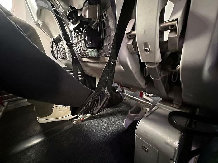 Passenger using an in-flight foot hammock under airplane seats showing coach budget travel essentials for comfort.