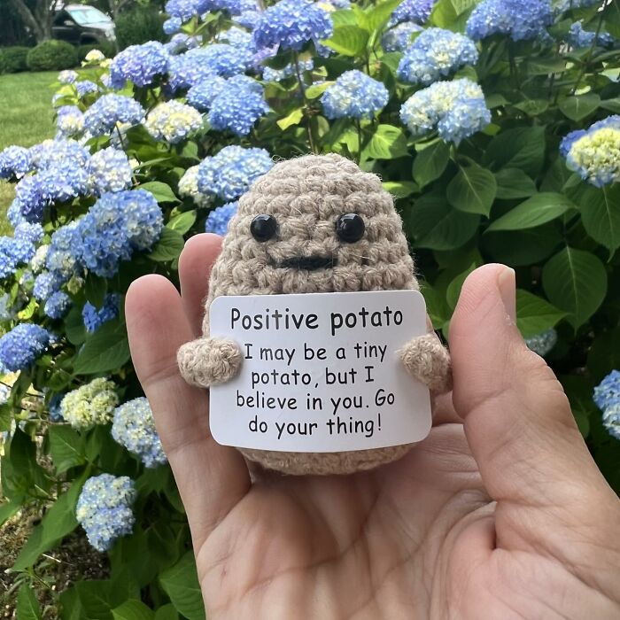 Hand holding a crocheted positive potato figure with inspiring note, perfect desk find for creating a Monday happy place.