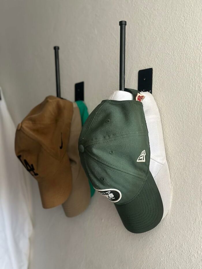 Several affordable baseball caps hanging on black wall hooks, popular Amazon finds for everyday use.