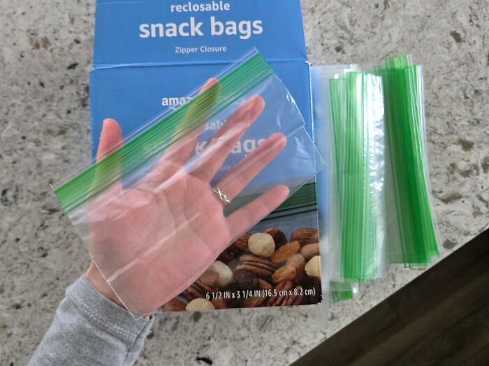 Clear reclosable snack bags with zipper closure held above a box on a kitchen countertop, Amazon Memorial Day sale item.