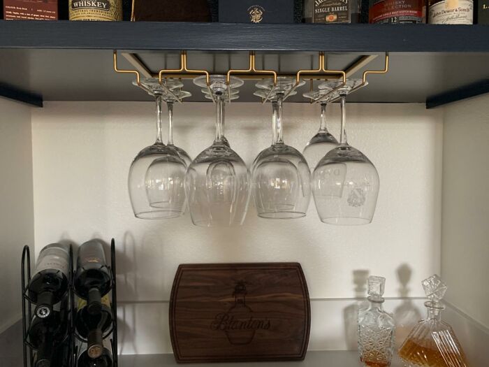 Wine glasses hanging in a shoebox kitchen bar area with bottles and decanters maximizing every square inch of space.