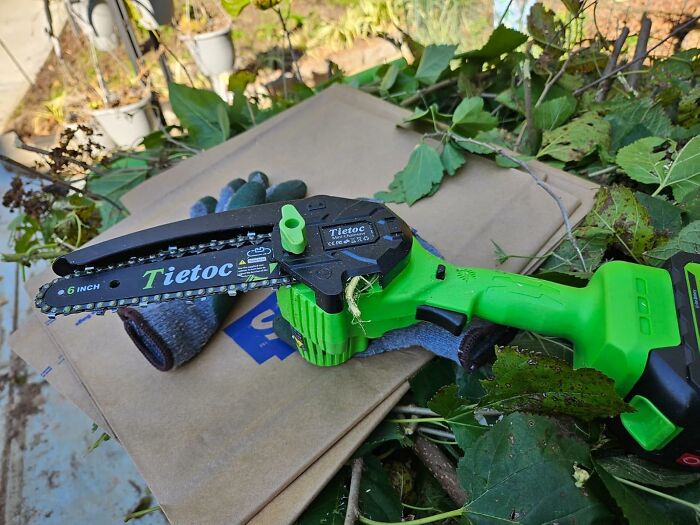 Compact green chainsaw resting on garden gloves and cardboard, ideal for Father's Day gifts and outdoor tool enthusiasts.