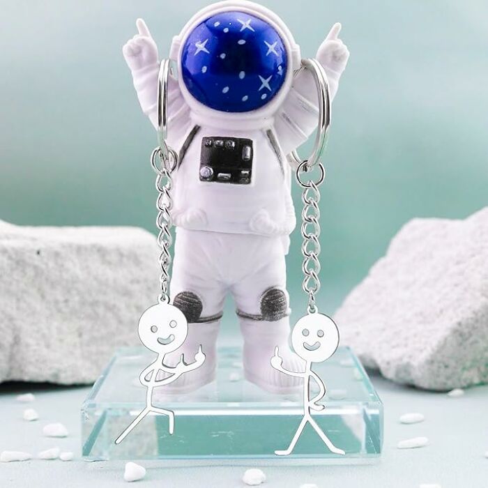 Silver stick figure keychains with playful gestures displayed on a space-themed astronaut stand, unique friendship gift idea.
