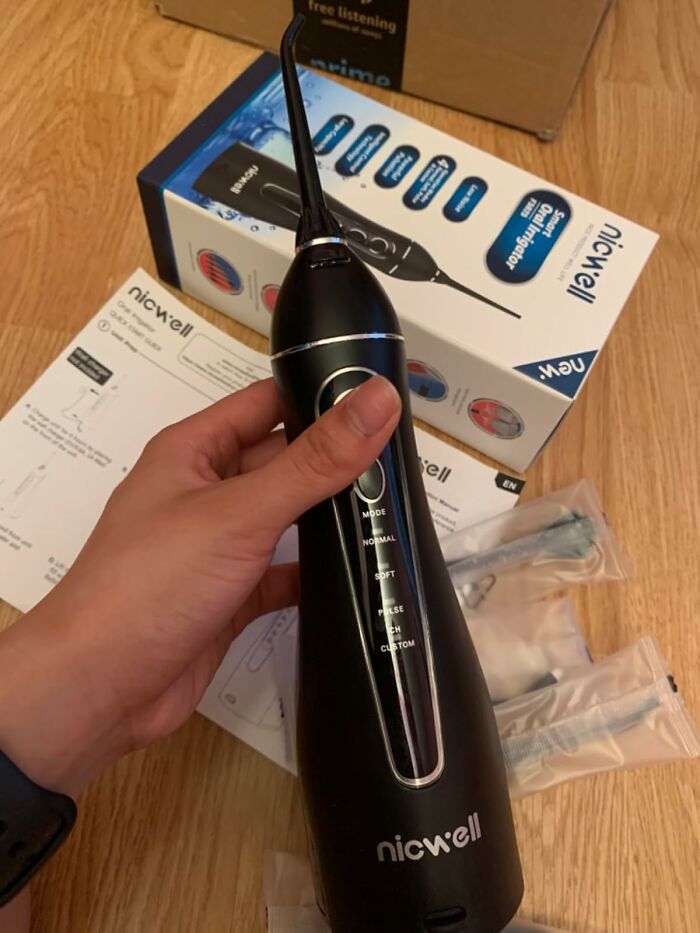 Hand holding a Nicwell water flosser with packaging and instruction manuals on a wooden surface, morning routine hack.