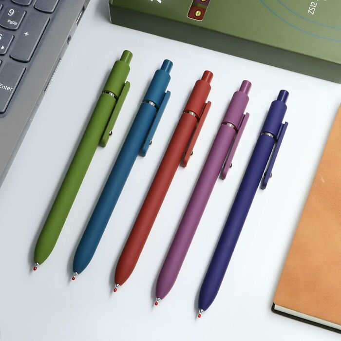 Colorful pens arranged on a desk alongside a laptop and notebook, ideal office supplies for a productive workspace.
