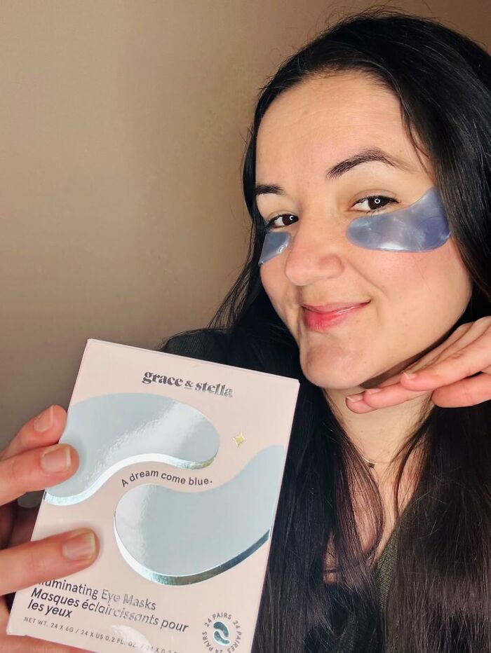 Woman wearing blue eye masks and holding a box of glowing under-eye masks, a popular affordable find on Amazon.