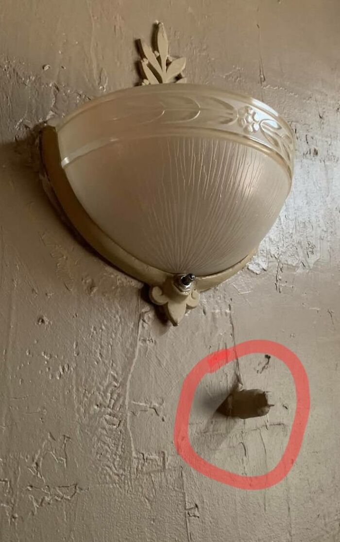 Old vintage light fixture on textured wall with a small circled hole, showcasing strange things found in homes.