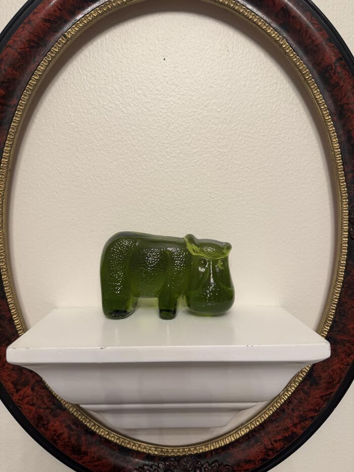 Green glass animal figurine displayed on a white shelf inside an ornate oval frame thrifted finds museum-worthy collectible