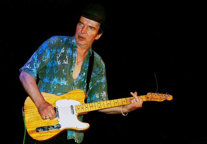 Male musician playing electric guitar on stage, representing notable people who passed away in 2025.