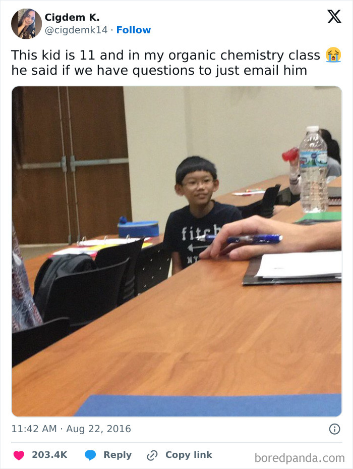 Young boy in classroom, sitting at desk with notebooks and water bottle, funny random meme capturing school moment.
