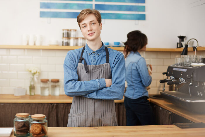 Young barista in apron standing behind counter, representing small decision that unexpectedly changed life forever.