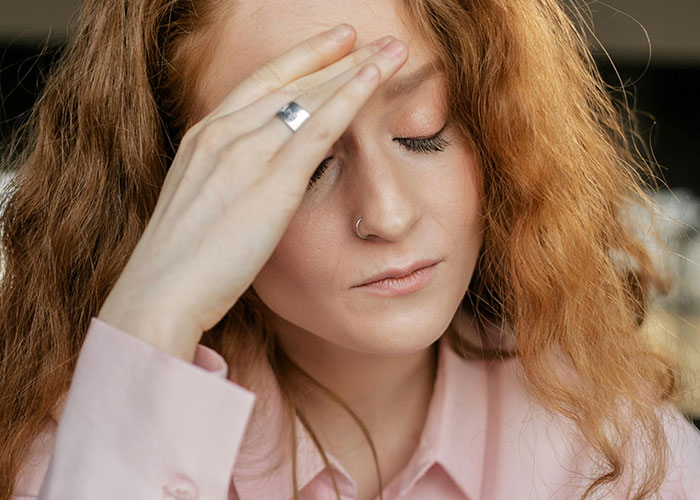 Young woman with red hair looks distressed, holding her forehead, reflecting trauma and relationship struggles.