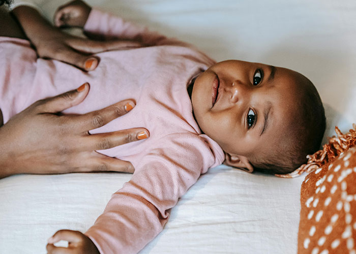 Baby lying on a bed wearing a pink outfit, with hands gently resting on their chest, showing entertaining facts concept.