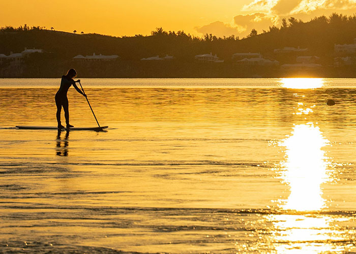 Person paddleboarding on calm water at sunset, illustrating best and worst things about living in their home country.