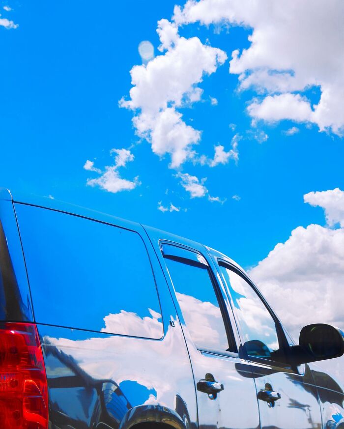 Shiny black car reflecting a vibrant blue sky with white clouds, showcasing creative photo edits that question reality.
