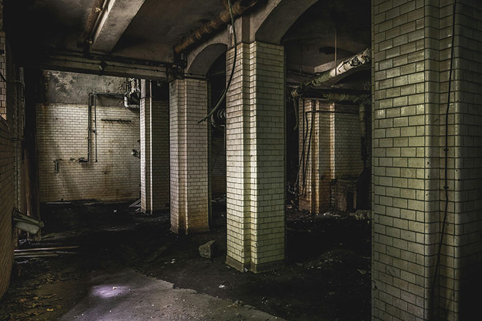 Dark abandoned basement with concrete pillars and dirty tiled walls evoking a scary gut feeling to leave now.