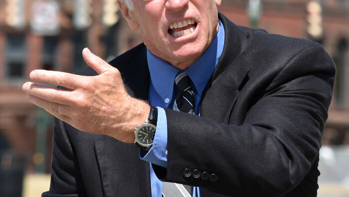 Angry man in suit gesturing with hand outdoors, representing harassment faced by woman with POTS using a car.