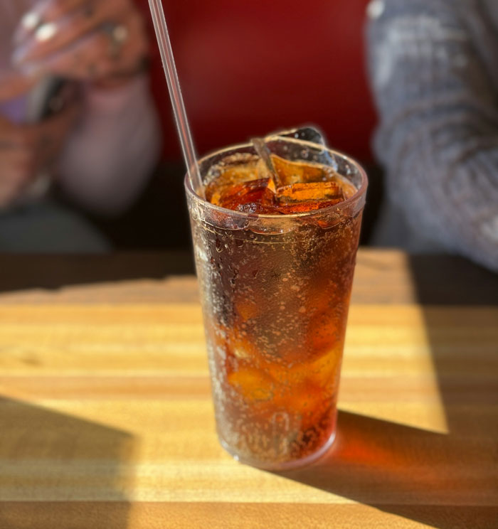 Glass of soda with ice and straw on a wooden table, illustrating one weird parenting rule topic discussion.