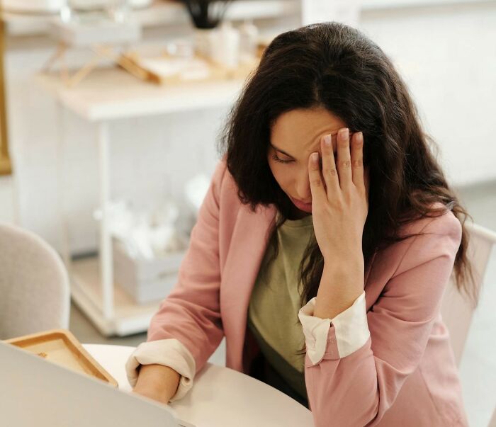 Woman in a pink blazer looking overwhelmed while working on a laptop, illustrating questioning reality and new facts concept.