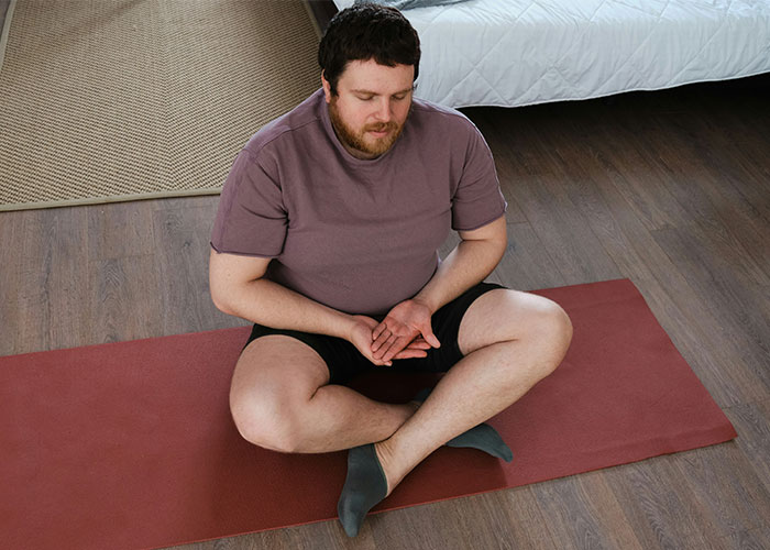 Man sitting cross-legged on a yoga mat, holding his wrist in discomfort, illustrating pathetic injuries concept.