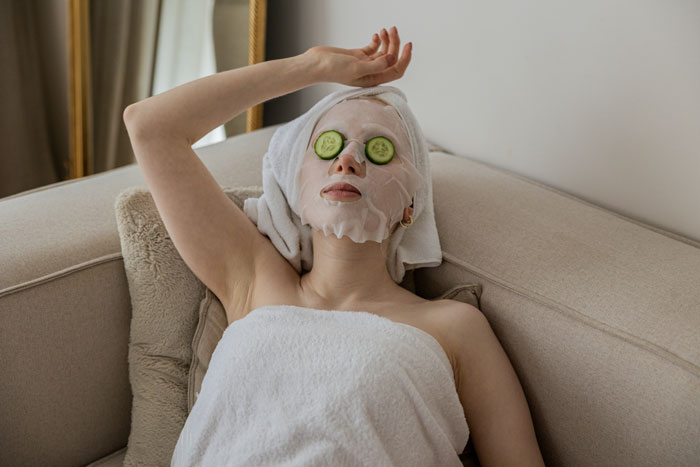 Woman with a face mask and cucumber slices on eyes relaxing on a couch illustrating weird habit raised poor concept.