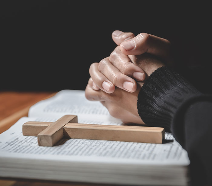 Hands clasped in prayer over an open Bible with a wooden cross, symbolizing faith and hope for baby's health.