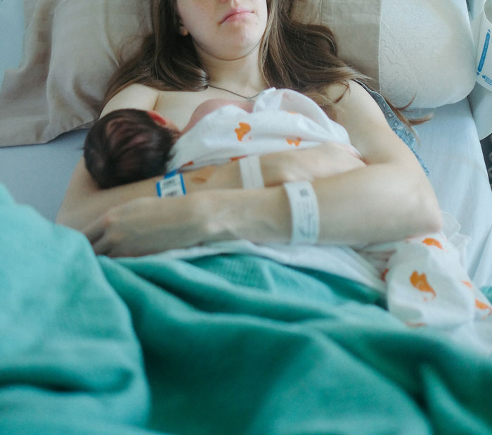 New mom holding newborn baby in hospital bed, illustrating the expensive cost of giving birth in the US.