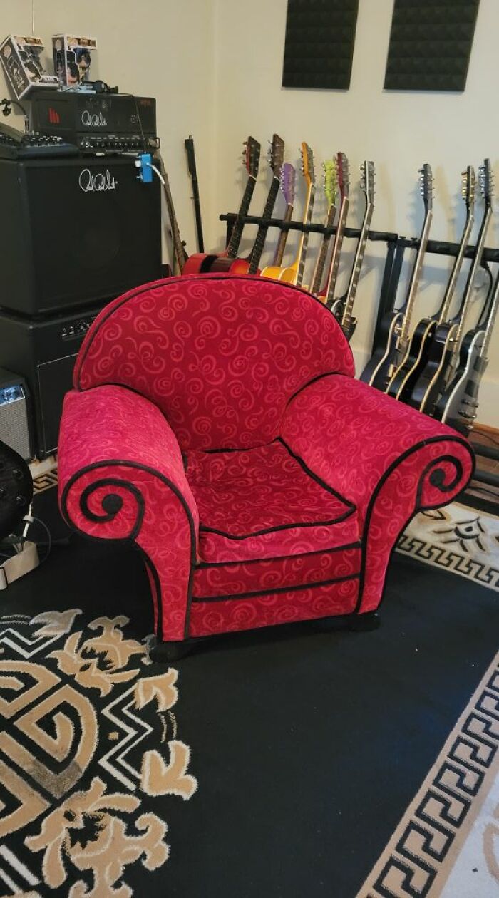 Bright red thrifted armchair with swirling patterns in a music room filled with guitars and amplifiers.