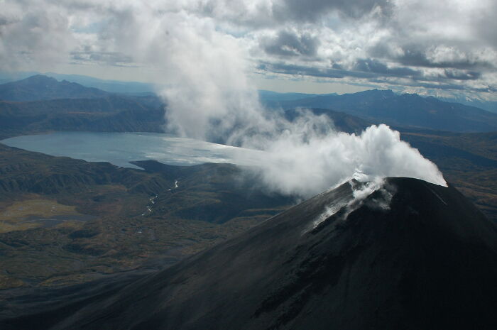 Aerial view of a smoking volcano surrounded by rugged terrain, showcasing hidden UNESCO gems in a remote natural landscape.