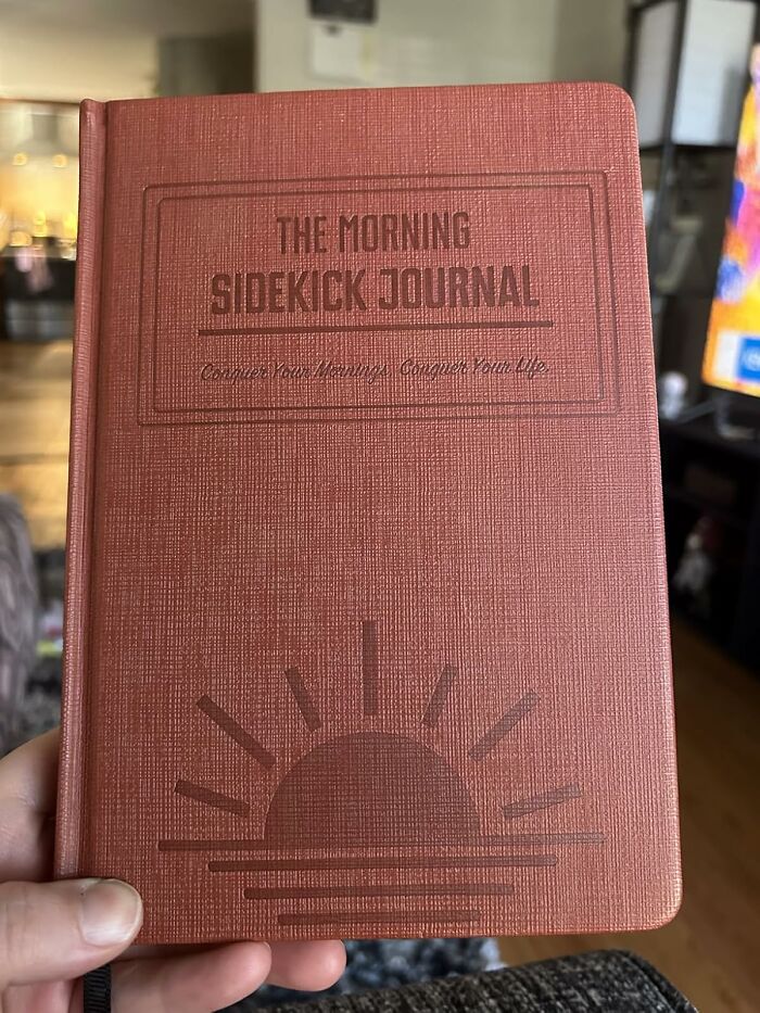 A person holding The Morning Sidekick Journal with a sunrise design, focusing on hacks to become a morning person.