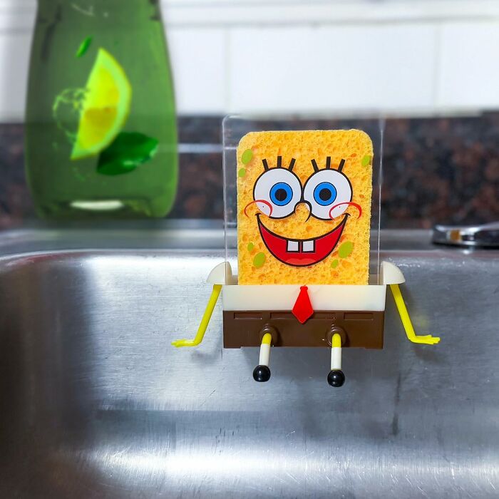 Kitchen gadget sponge holder shaped like a cartoon character sitting on a metal sink, adding fun to kitchen tools.