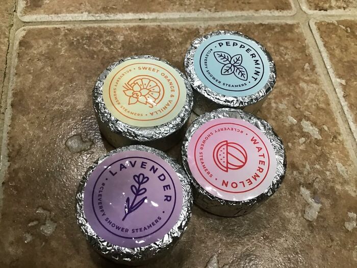 Four colorful shower steamers labeled peppermint, watermelon, lavender, and sweet orange on a tiled surface for an instant mood lift.