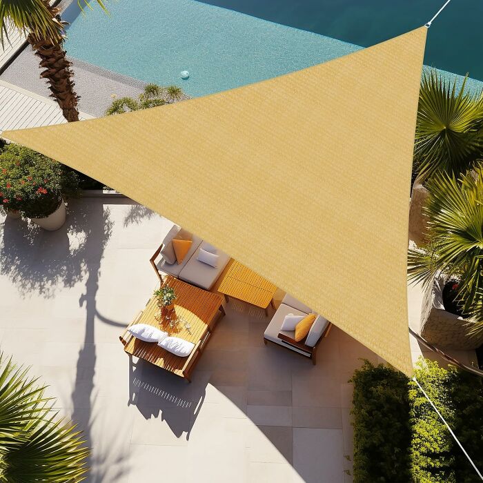 Backyard outdoor upgrade with a triangular sunshade covering lounge chairs next to a pool surrounded by palm trees.