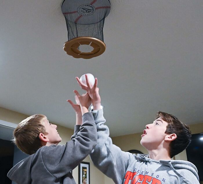 Two boys reaching to catch a baseball in a ceiling hoop, showcasing one of the weirdly wonderful finds for beige-loving friends.