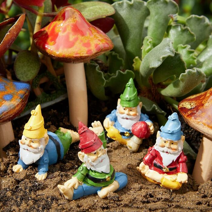 Colorful garden gnome figurines relaxing among vibrant ceramic mushrooms and green succulent plants in soil.