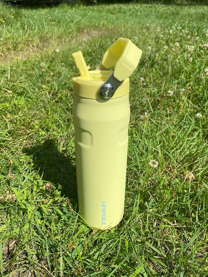 Yellow reusable water bottle with flip-top lid standing on green grass, ideal for warm weather finds to stay hydrated.