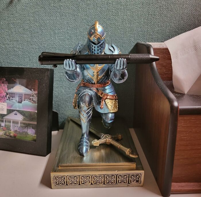 Kneeling knight figurine holding a large pen, displayed among weirdly wonderful finds on a desk with photos and tissues.