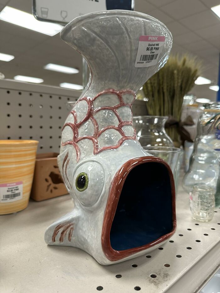 Ceramic fish sculpture with wide open mouth, a quirky thrifted find displayed on a store shelf among other items.