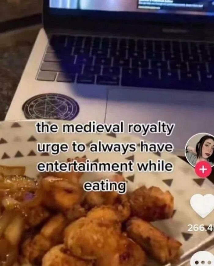 Close-up of a laptop and plate of food with text about medieval royalty showing chaotic memes humor during a meal.