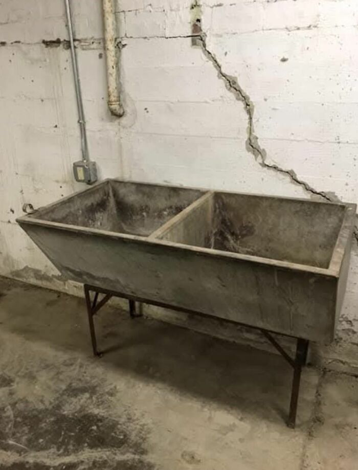 Old concrete utility sink in a basement with c*****d walls, showing strange things found in homes with hidden pasts.
